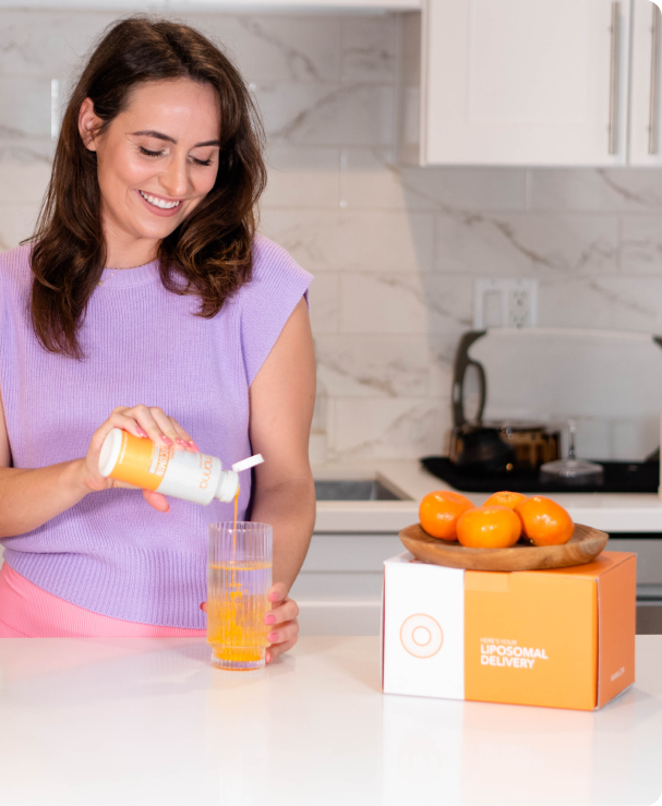 A woman is pouring Liposomal Curcumin into a glass in her kitchen