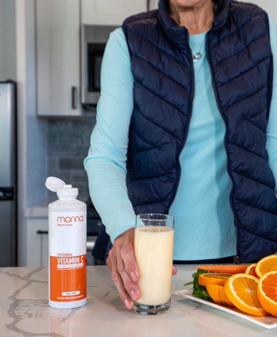 A woman is pouring Liposomal Curcumin into a glass in her kitchen